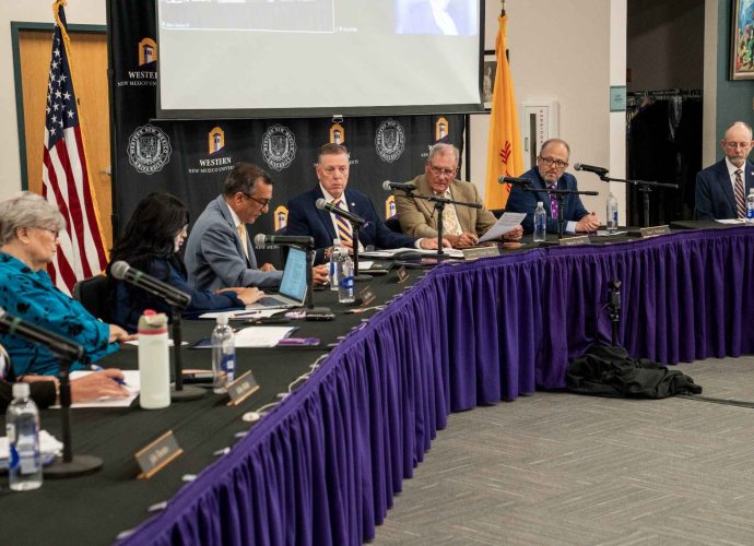 Western New Mexico University regents and administrators seated at tables with microphones during a board meeting.
