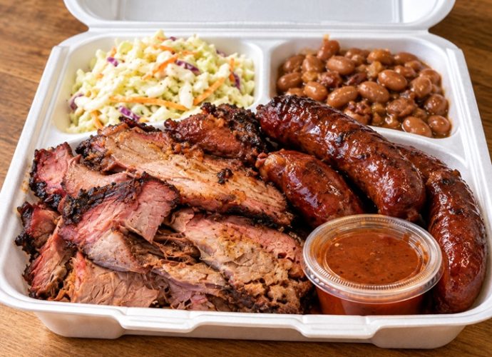 A takeout meal of klobase, barbecue meat, coleslaw and pinto beans with a cup of BBQ sauce.