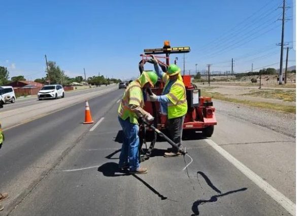 NMDOT road maintenance crew performing pavement sealing work on a highway.