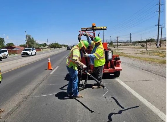 NMDOT road maintenance crew performing pavement sealing work on a highway.